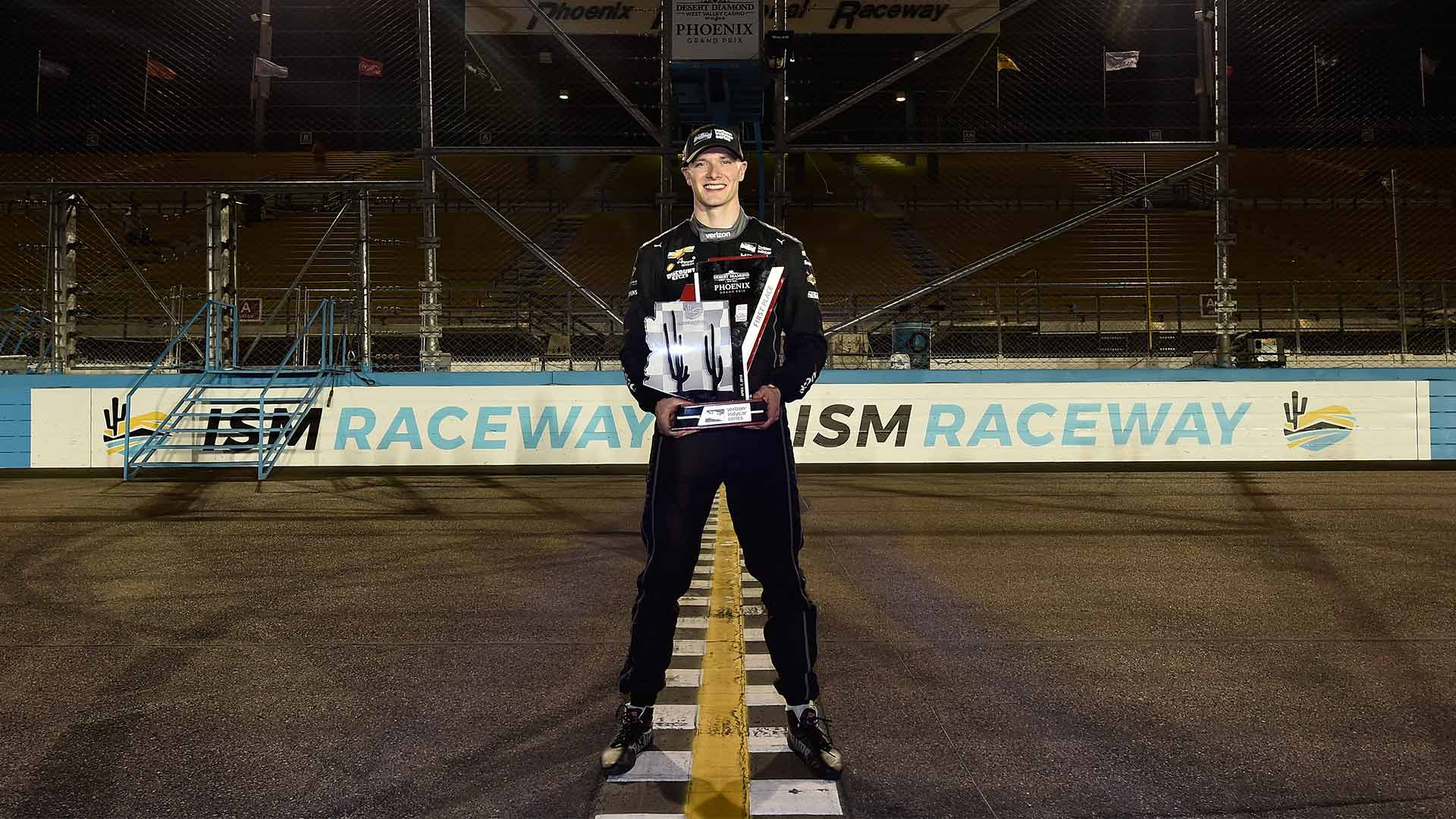 Josef Newgarden stands over the start/finish line with his trophy